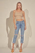 Woman wearing a beige crop top and light blue jeans against a plain background