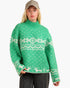 A woman wearing a green knit sweater with a white Nordic fair isle pattern, paired with a beige baseball cap and dark gray jeans, against a plain white background.