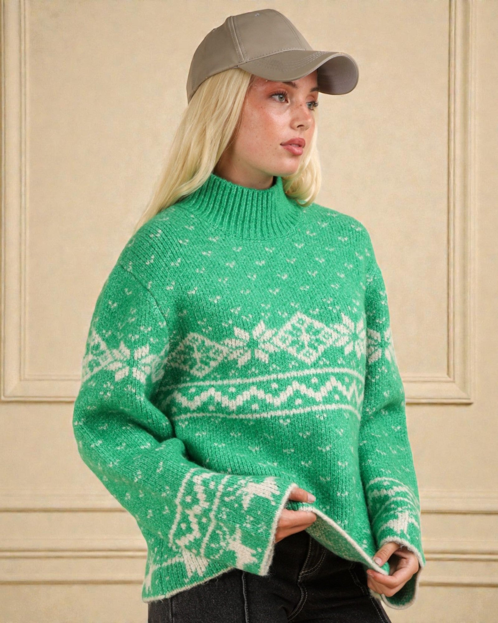 Person wearing a green sweater with white patterns and a gray cap against a beige wall.