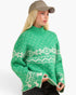 A woman wearing a green knit sweater with a cream Nordic pattern, paired with a beige baseball cap and dark jeans, shown against a plain white background.