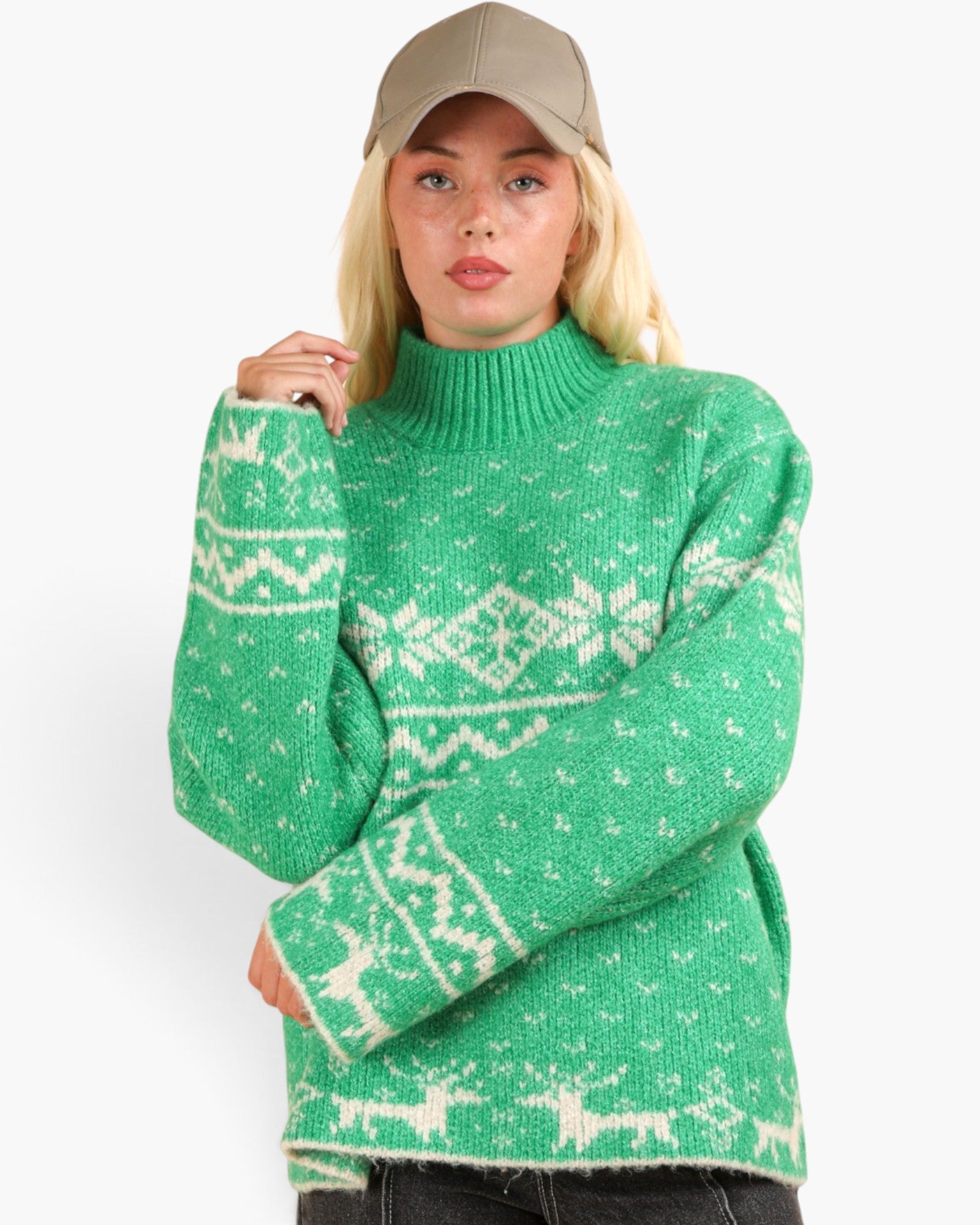 A woman wearing a green knit sweater with a white Nordic pattern and a beige baseball cap, photographed against a plain light gray background.
