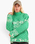 A woman wearing a green knit sweater with a white Nordic pattern and a beige baseball cap, photographed against a plain light gray background.