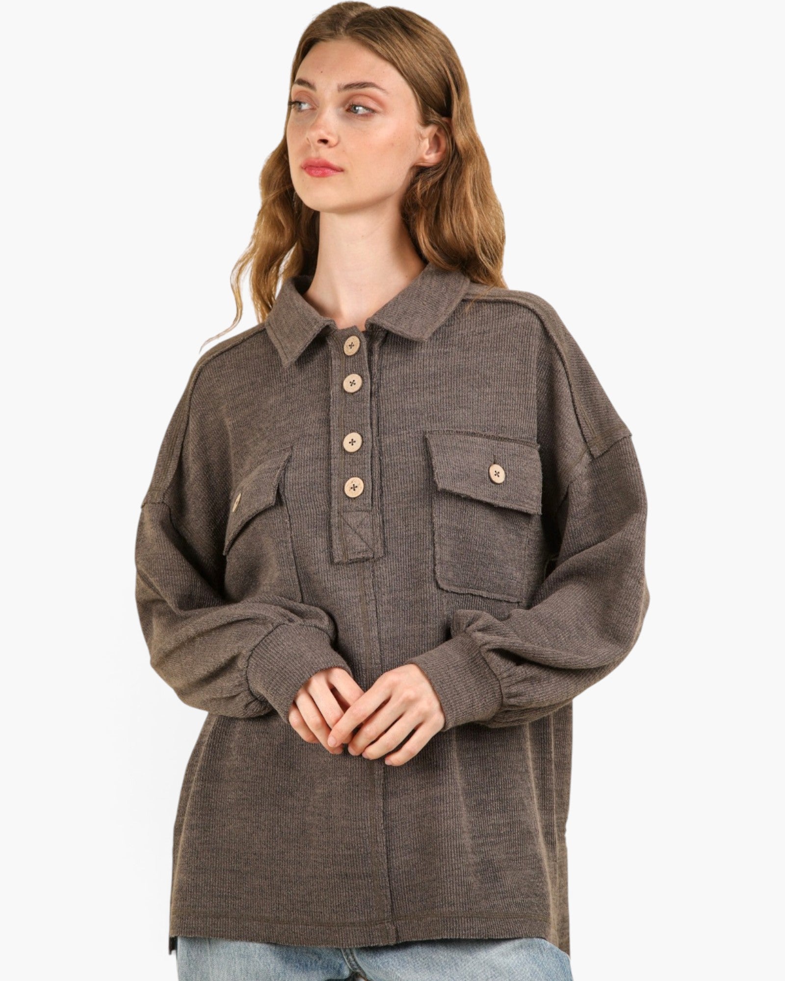 A woman wearing a dark brown textured button-up shirt jacket with chest pockets, paired with light blue jeans, against a plain white background.