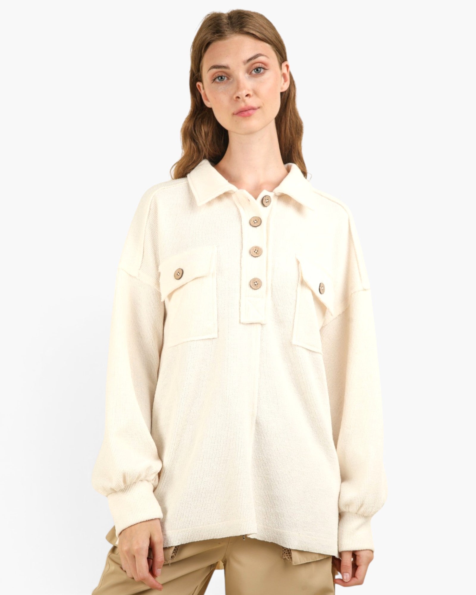 A woman modeling a cream-colored long-sleeve button-up shirt with flap chest pockets and tan pants, set against a plain light gray background.