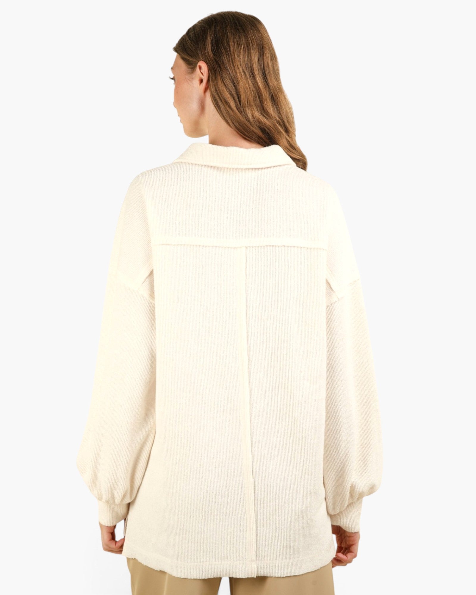 A woman shown from the back wearing a cream-colored, long-sleeved button-up shirt with a relaxed fit and a small collar, paired with beige pants against a plain white background.