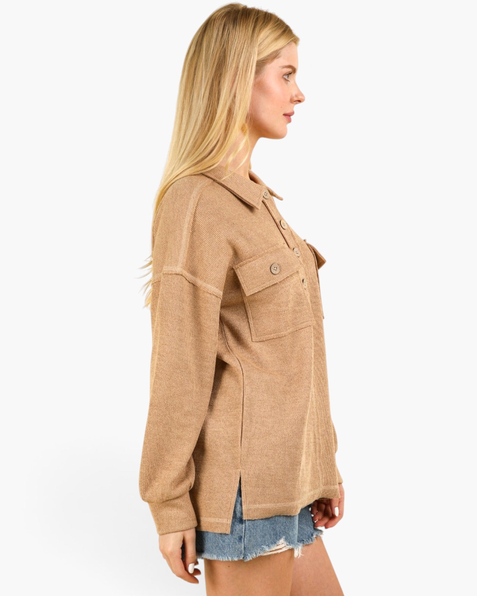 A woman shown in side profile wearing a tan long-sleeve button-front overshirt with flap chest pockets and denim shorts against a plain light gray studio background.