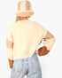 A person shown from the back wearing a cream and tan knit sweater with brown elbow patches, a matching beige bucket hat, and light blue jeans against a plain white background.