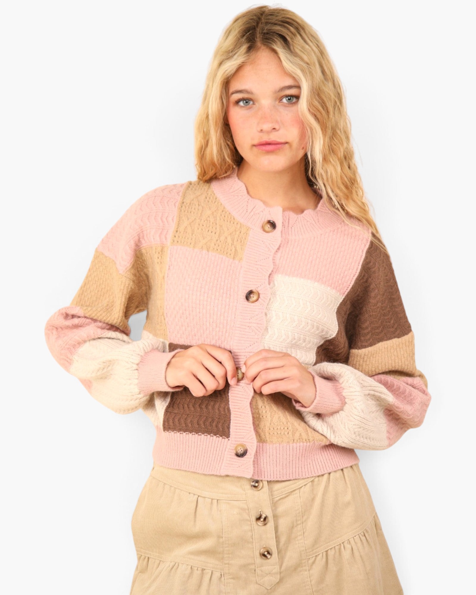 A young woman wearing a pastel color-block knit cardigan with pink, beige, and brown panels, paired with a beige skirt, against a plain white background.