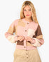 A young woman wearing a pastel color-block knit cardigan with pink, beige, and brown panels, paired with a beige skirt, against a plain white background.