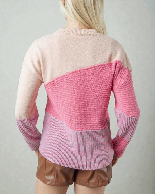 Person wearing a pink and beige sweater with brown shorts on a plain background