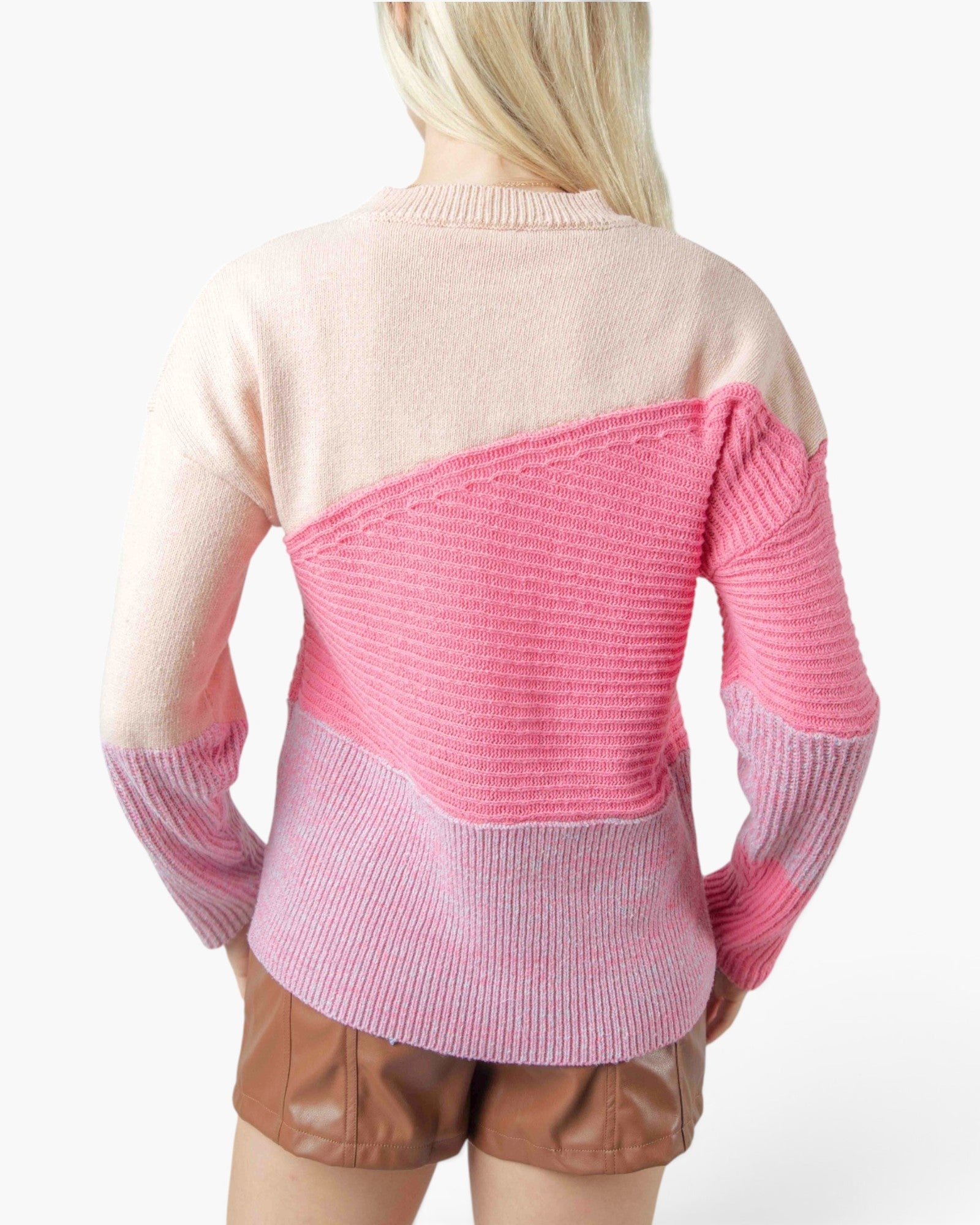 A woman shown from the back wearing a color-block knit sweater with a light beige upper section, a bright pink middle section, and a pinkish-purple lower section, paired with brown shorts against a plain white background.