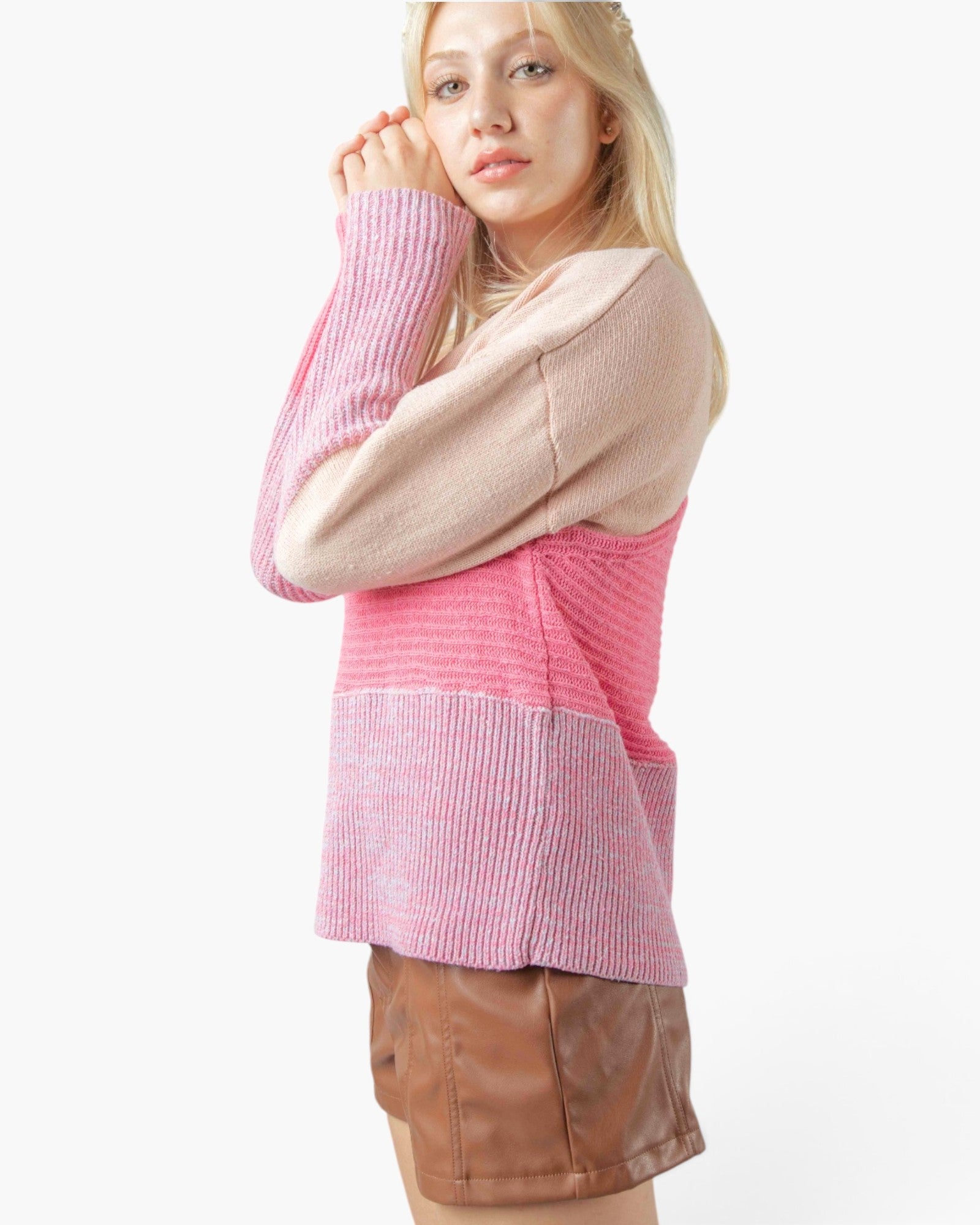 A woman wearing a color-block knit sweater with a beige upper section, pink middle section, and pink-and-white vertically ribbed lower section, paired with brown shorts, against a plain white background.