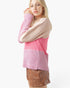 A woman wearing a color-block knit sweater with a beige upper section, pink middle section, and pink-and-white vertically ribbed lower section, paired with brown shorts, against a plain white background.