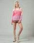Woman wearing a pink and beige sweater with brown shorts on a gray background