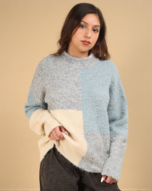 Woman wearing a color-blocked sweater holding a beige blanket against a beige background