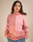 Woman wearing a pink and peach patchwork sweater against a beige background