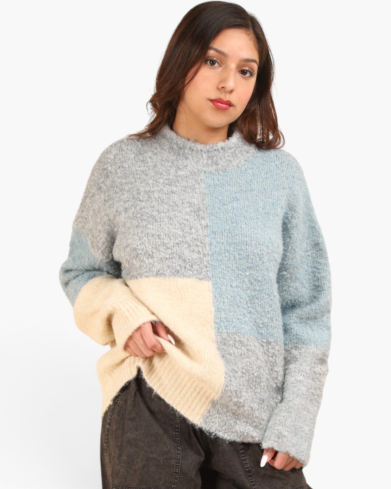 A woman wearing a fuzzy color-block knit sweater with a light gray and pale blue upper body and a cream lower body, paired with dark gray pants, against a plain white background.