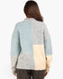 A woman viewed from behind wearing a fuzzy knit patchwork cardigan with blocks of light blue, heather gray, and cream, paired with dark brown pants against a plain white background.