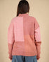 Person wearing a pink and peach color-blocked sweater against a beige background