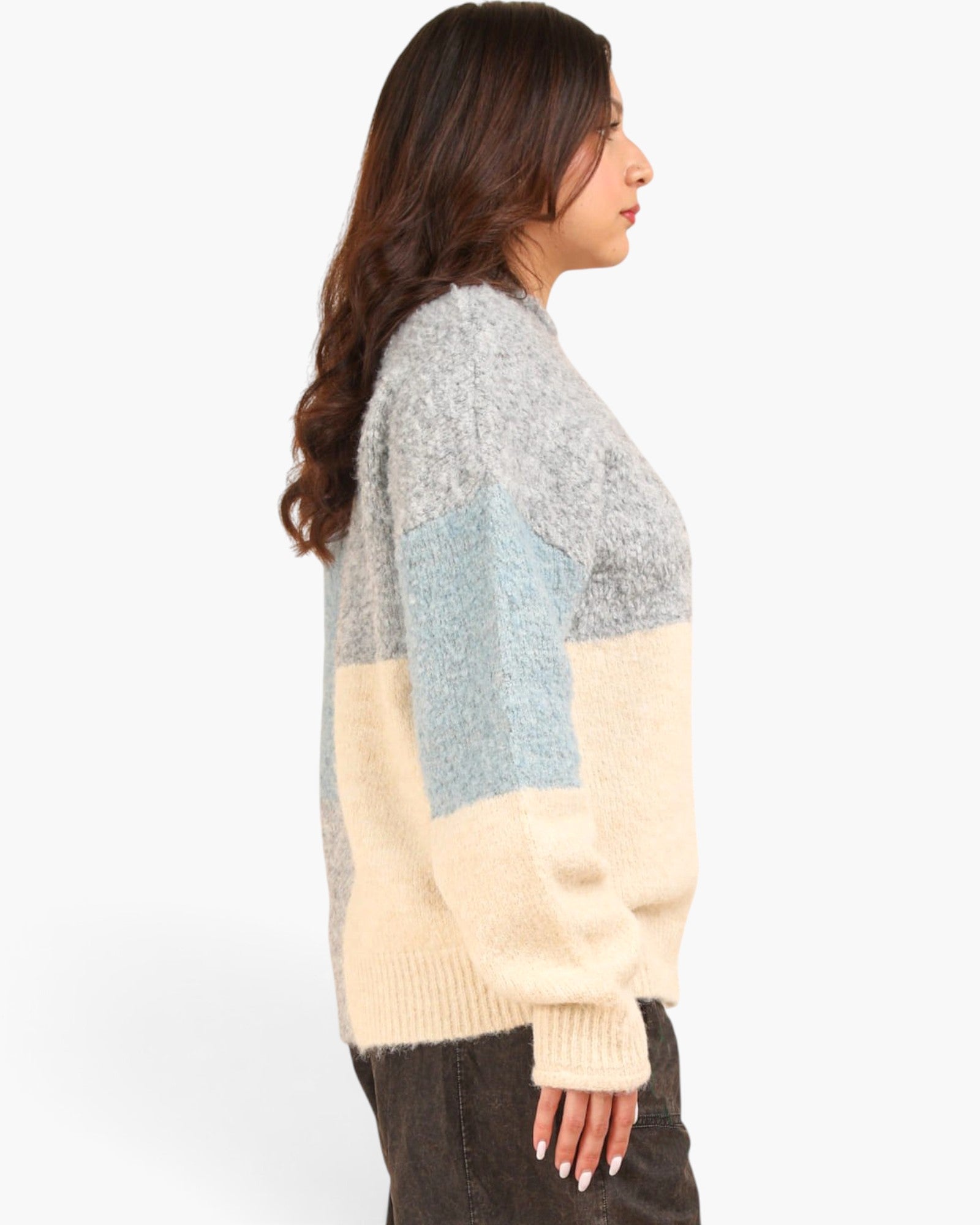 A woman wearing a fuzzy color-block knit sweater with gray, light blue, and cream panels, paired with dark pants, photographed against a plain white studio background.
