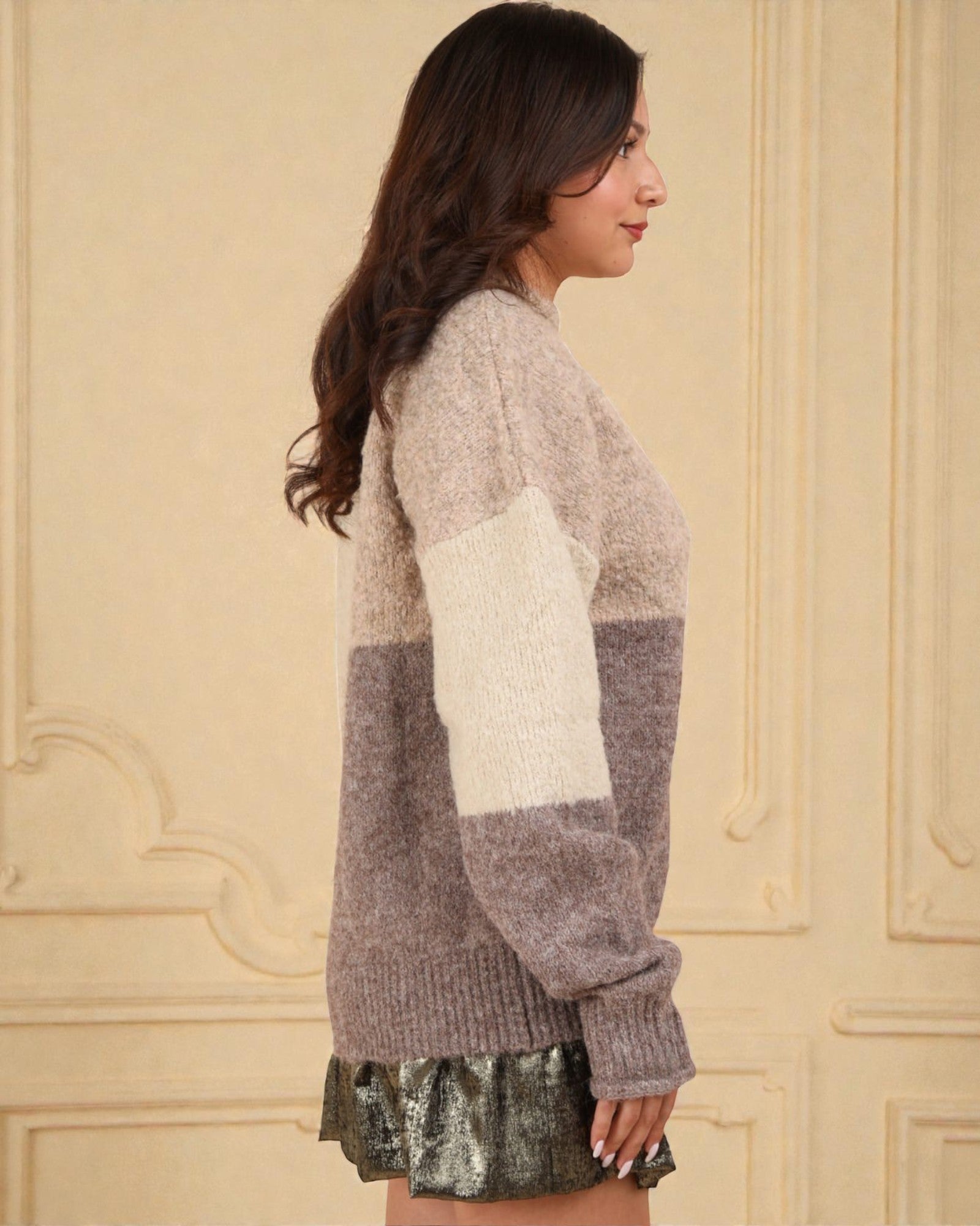 Woman wearing a two-tone sweater with a beige and gray pattern against a beige wall.
