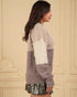 Woman wearing a two-tone sweater with a beige and gray pattern against a beige wall.