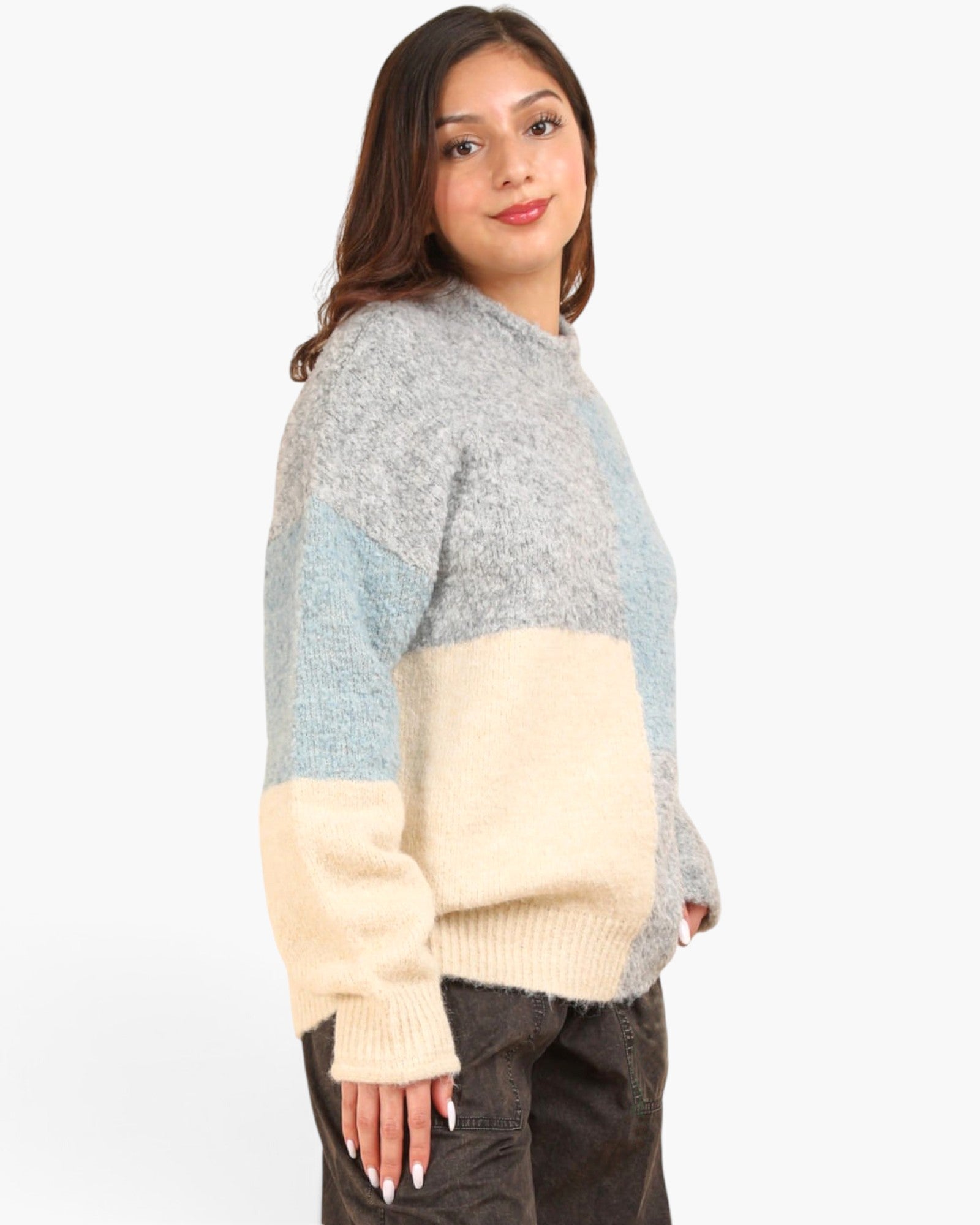 A woman wearing a fuzzy color-block knit sweater with gray, light blue, and cream panels, paired with dark pants, photographed against a plain white studio background.