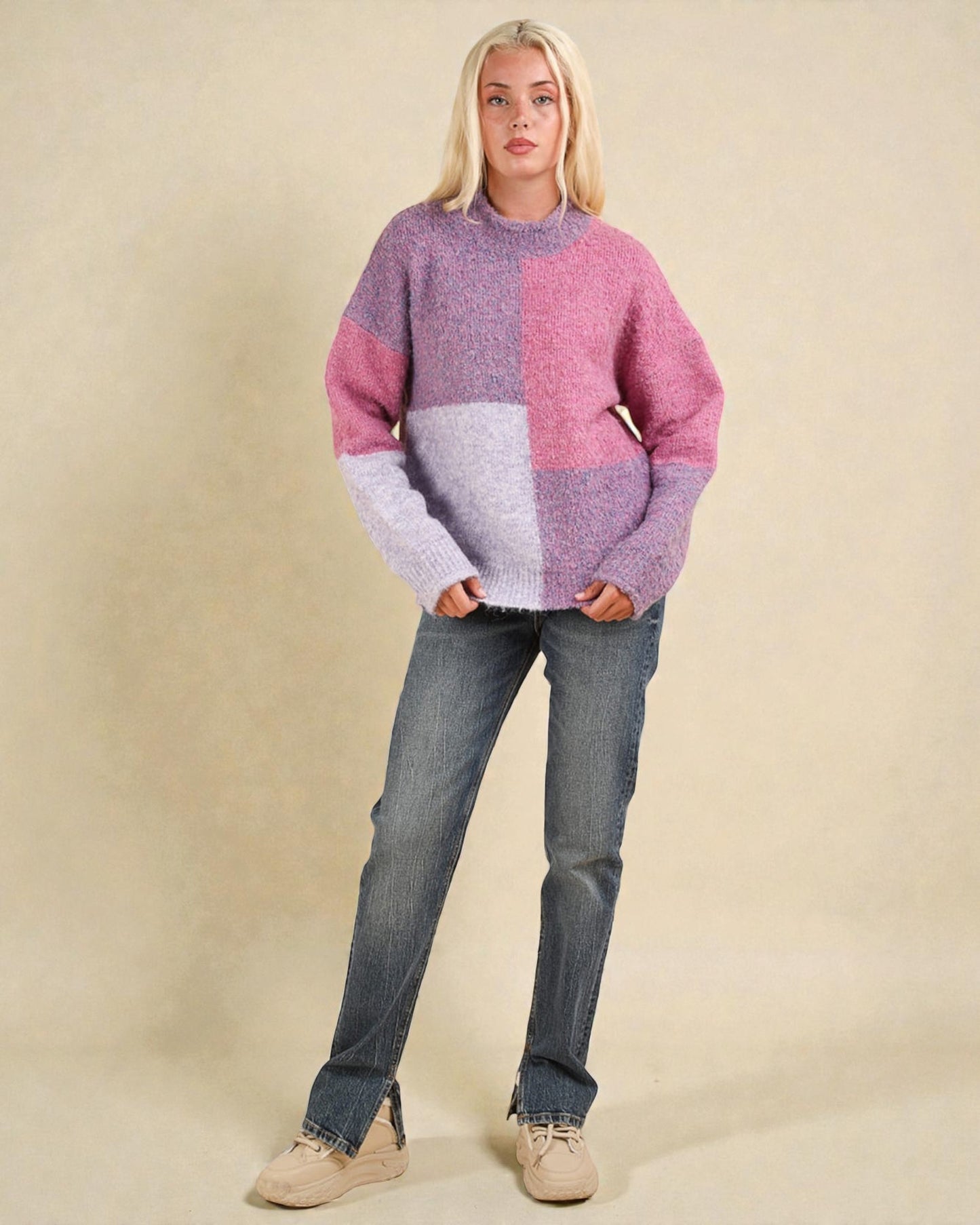 Person wearing a pink and purple sweater with blue jeans on a beige background