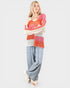 Woman wearing a colorful patterned sweater and light blue pants on a white background
