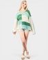 Woman wearing a green and white patterned sweater with denim shorts on a white background