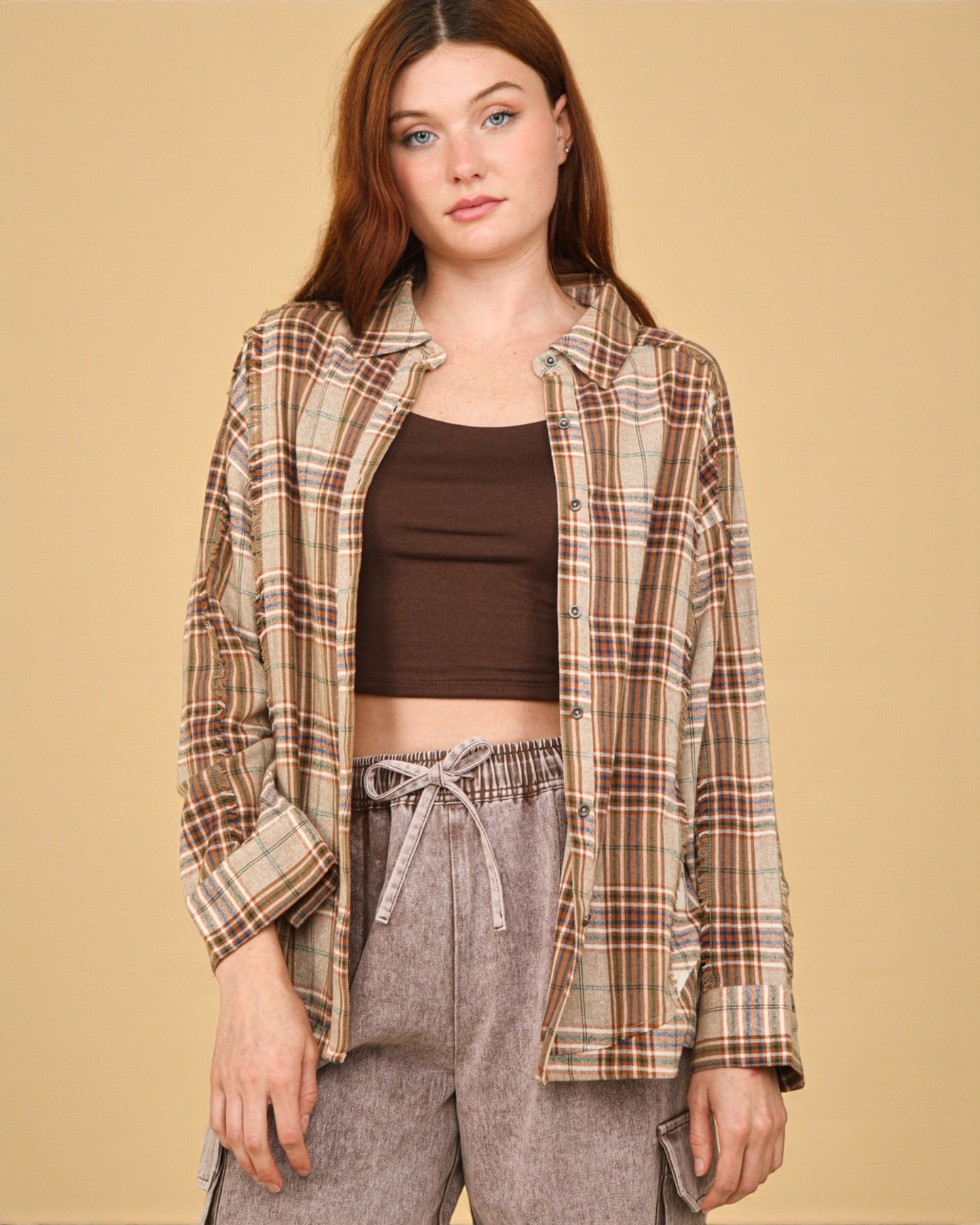 Woman wearing a plaid shirt over a brown top and gray pants on a beige background