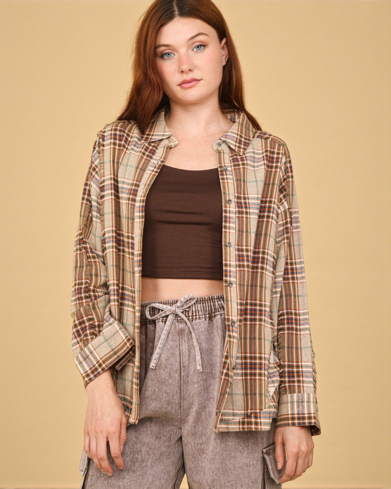 Woman wearing a plaid shirt over a brown top and gray pants on a beige background