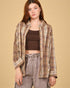Woman wearing a plaid shirt over a brown top and gray pants on a beige background
