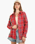 A woman wearing a red and blue plaid button-up shirt with distressed denim shorts and a beige baseball cap, photographed against a plain light gray background.