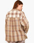 A woman shown from the back wearing an oversized plaid button-up shirt in beige, brown, and cream tones, paired with gray pants, against a plain light gray background.