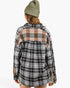 A person shown from the back wearing a long-sleeve plaid flannel shirt with a black, white, and gray base and a tan plaid yoke across the shoulders, paired with an olive green beanie against a light gray studio background.