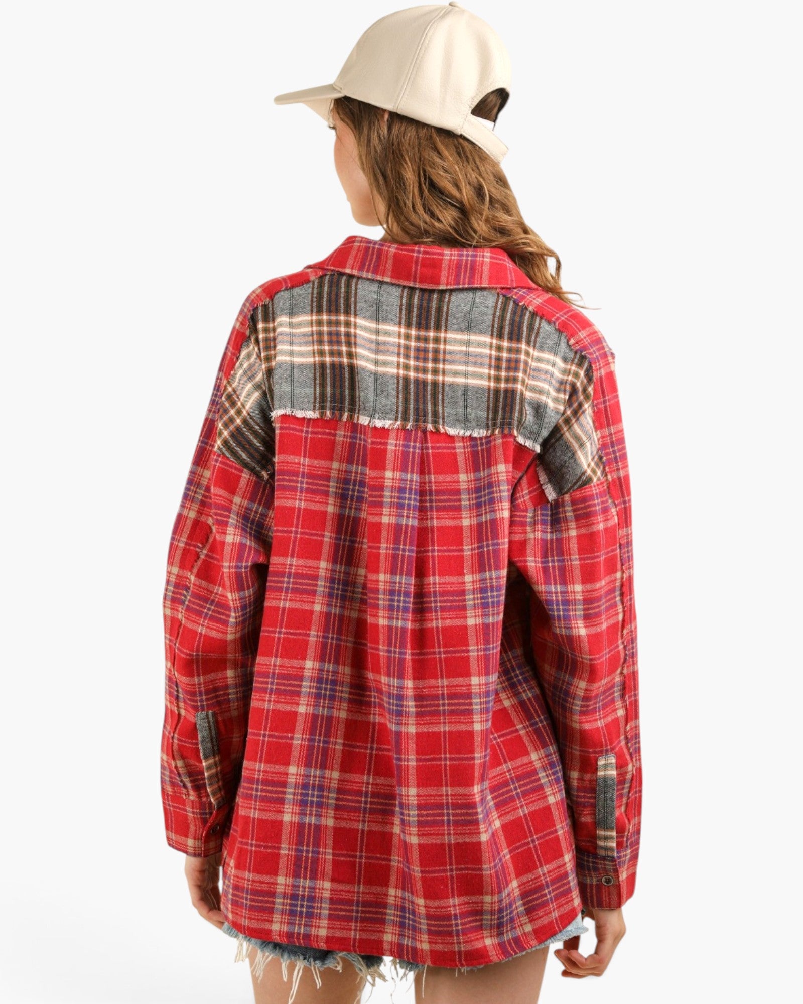 A woman shown from the back wearing a red plaid button-up shirt with a contrasting gray and black plaid yoke panel, paired with a cream baseball cap, against a plain white background.