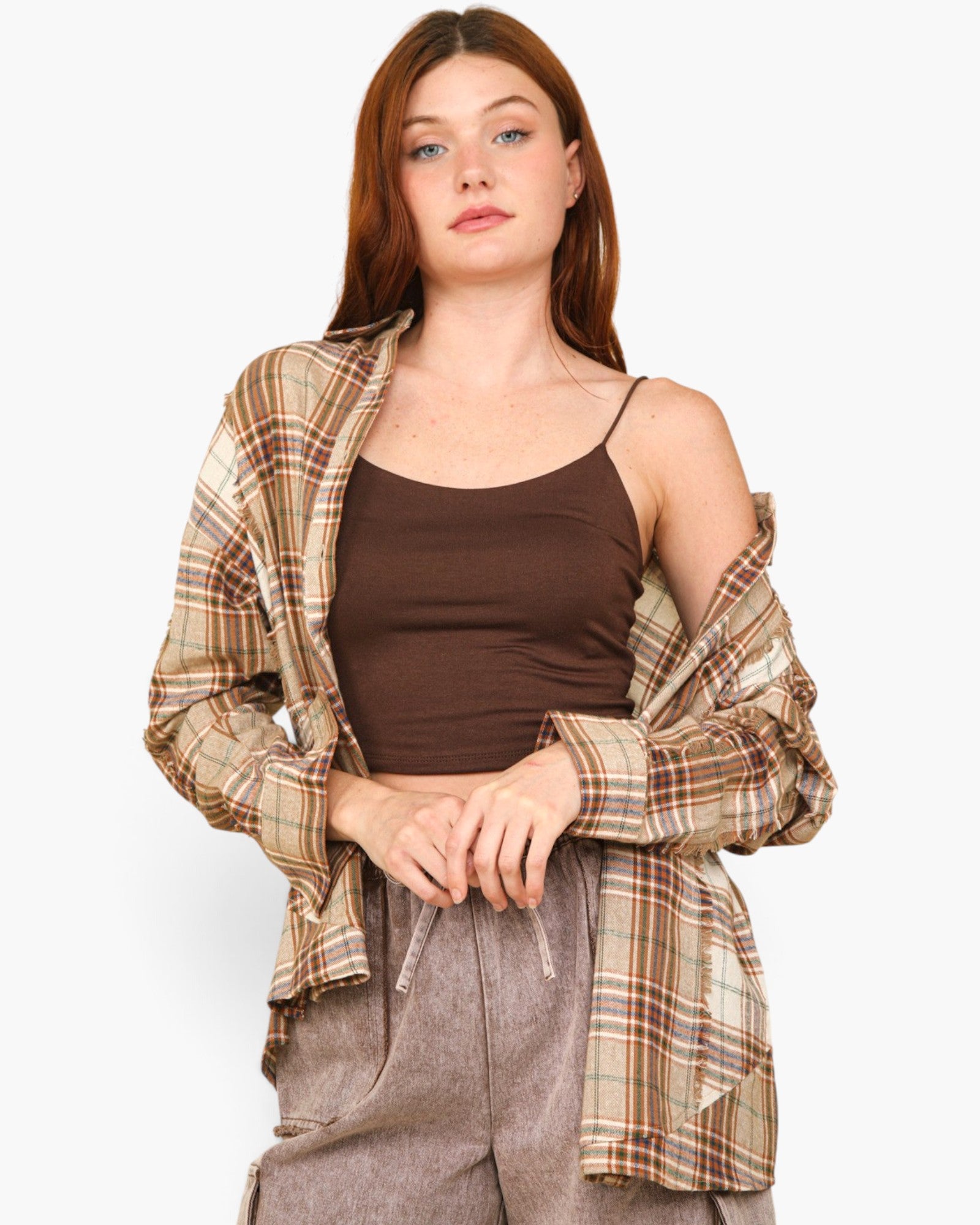 A woman modeling a brown ribbed camisole tank top, styled with an open beige and brown plaid flannel shirt and gray drawstring pants against a light gray background.