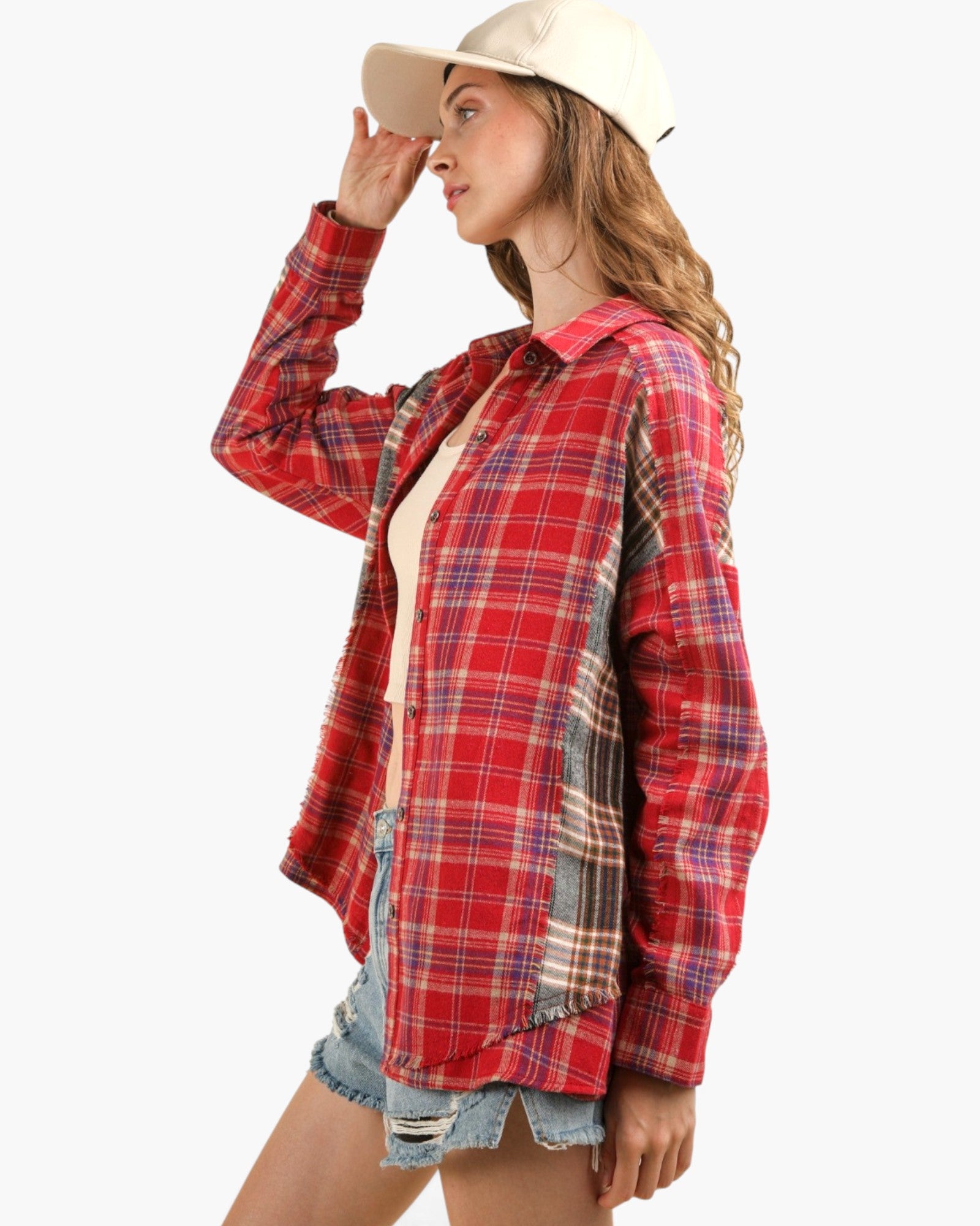 A woman wearing a red plaid button-up flannel shirt over a cream tank top, paired with denim shorts and a cream baseball cap, shown against a plain light gray background.