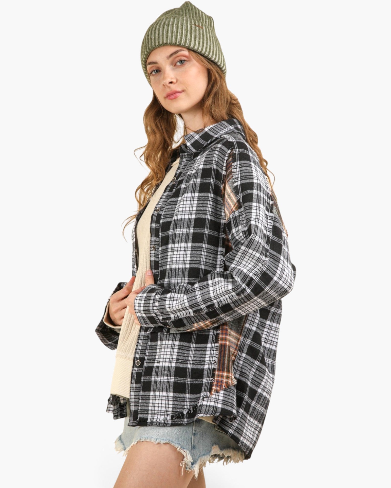 A woman wearing a black, white, and gray plaid button-up shirt over a cream undershirt, paired with a green ribbed beanie and denim shorts, photographed against a solid white background.