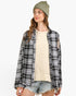 A woman wearing a black and white plaid distressed flannel shirt over a cream ribbed sweater, paired with denim shorts and a green striped beanie, against a plain white background.