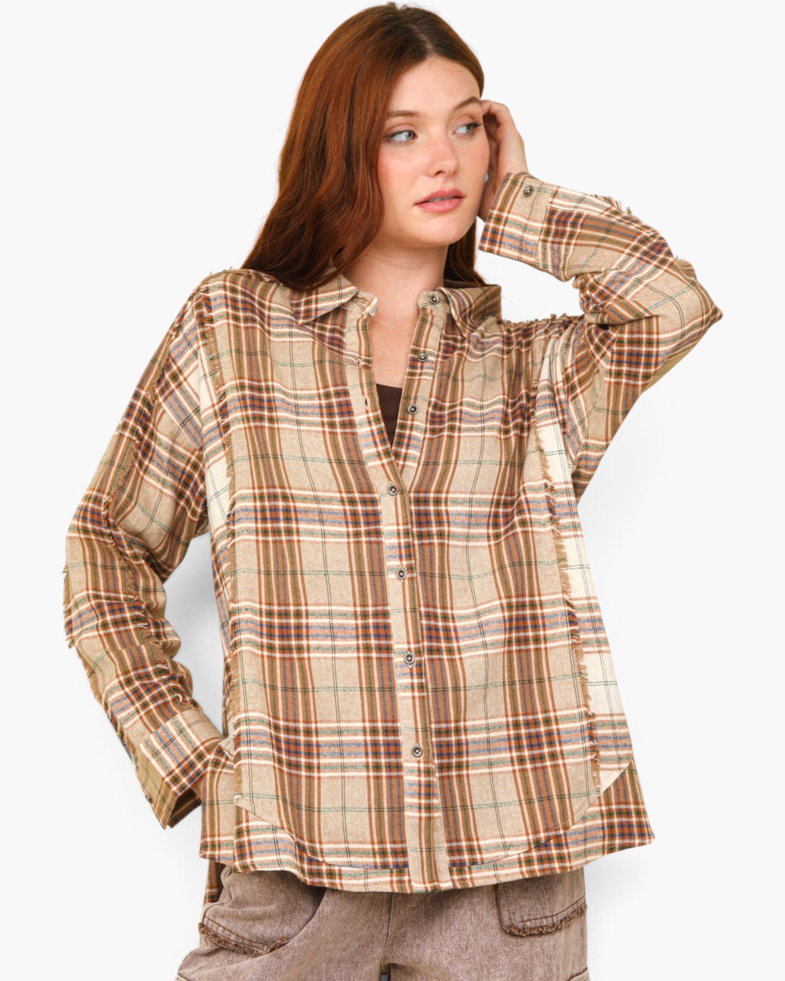 A woman wearing a beige and brown plaid button-up shirt, paired with brown pants, against a plain light gray background.