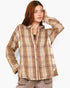 A woman wearing a beige and brown plaid button-up shirt, paired with brown pants, against a plain light gray background.