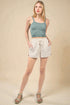 Woman wearing a green tank top and beige shorts against a beige background