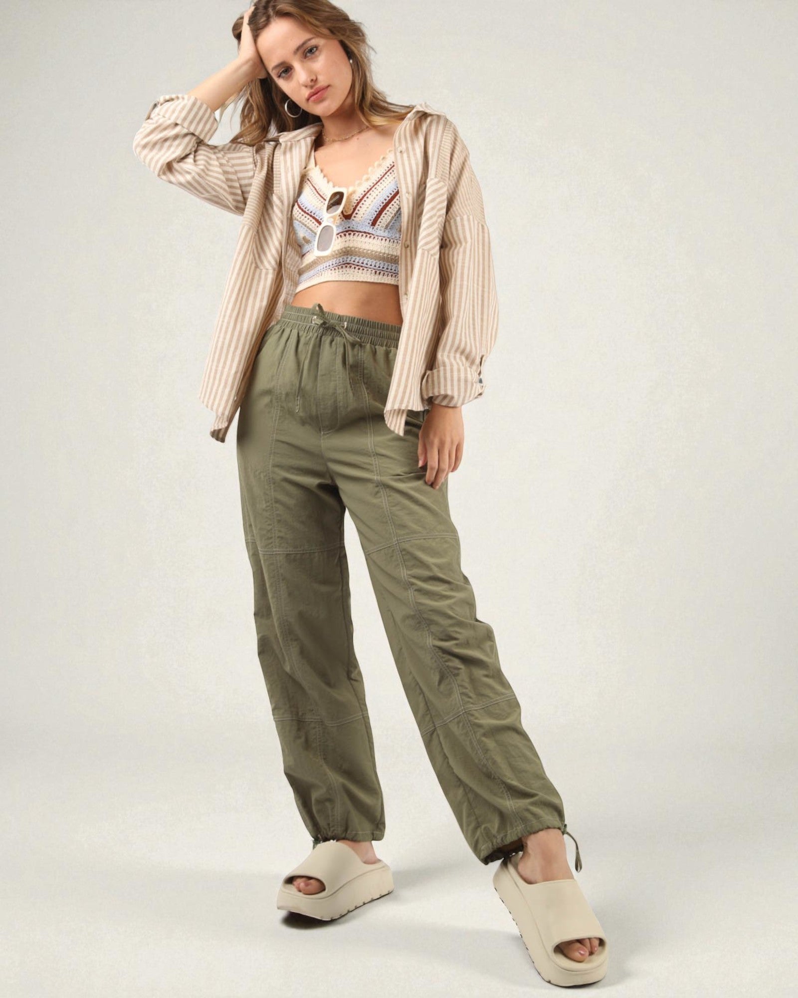 Woman wearing a striped shirt, crop top, and green pants on a white background