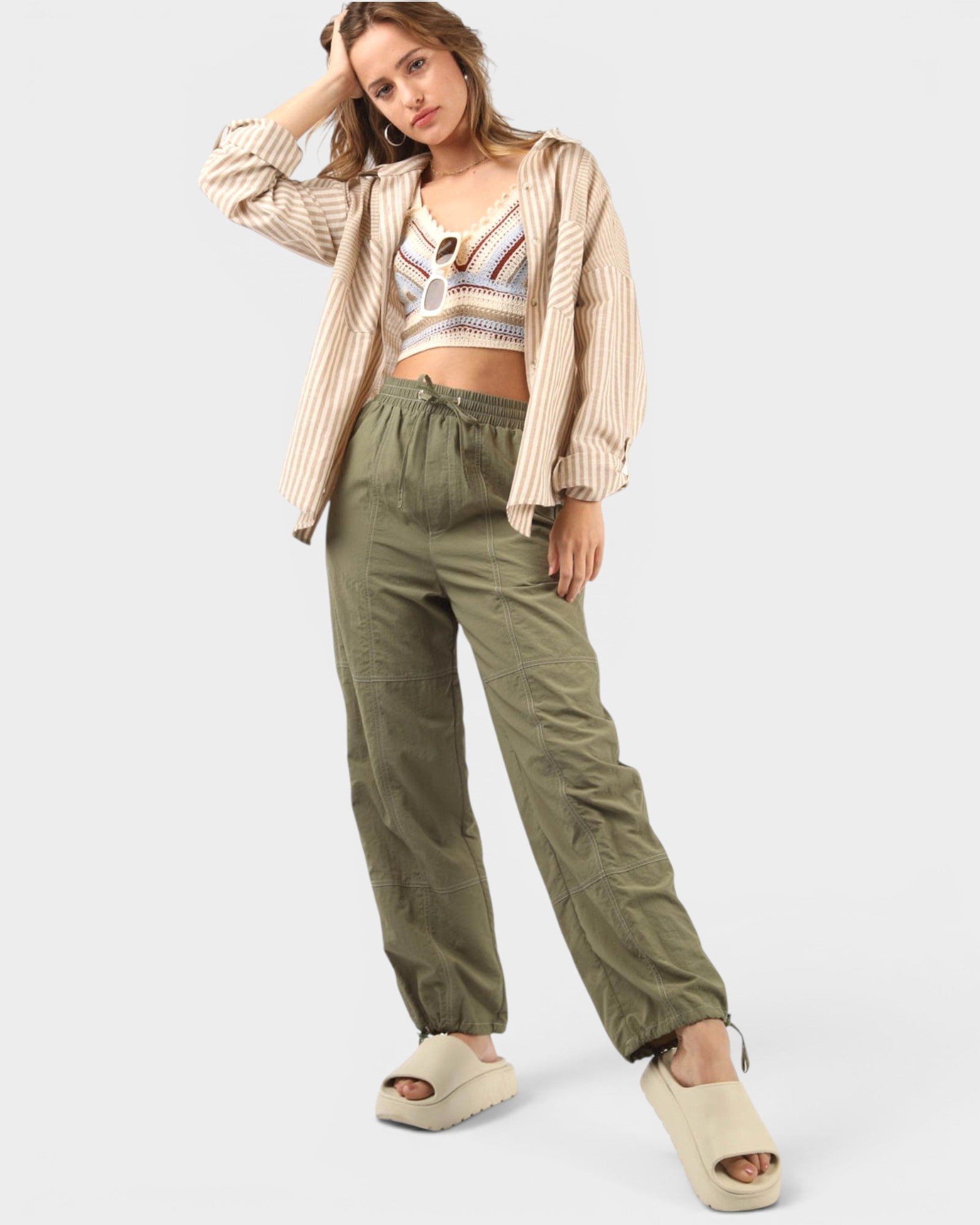 Woman wearing a beige jacket, patterned top, and green pants on a white background