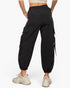 Black cargo jogger pants with side flap pockets and drawstring details, shown on a model from the back wearing beige sneakers against a light gray background.