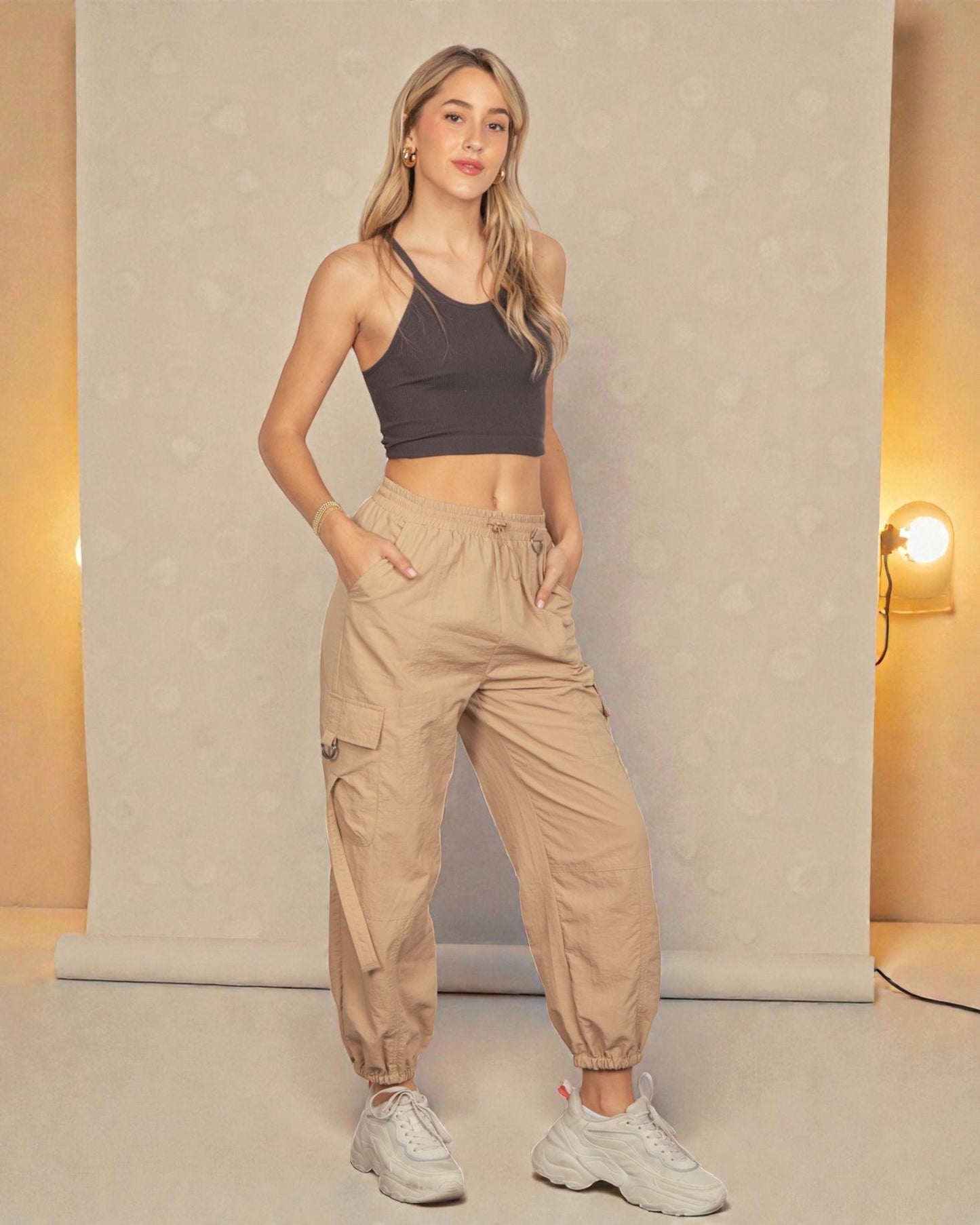 Woman wearing a dark sports bra and beige cargo pants in a neutral setting