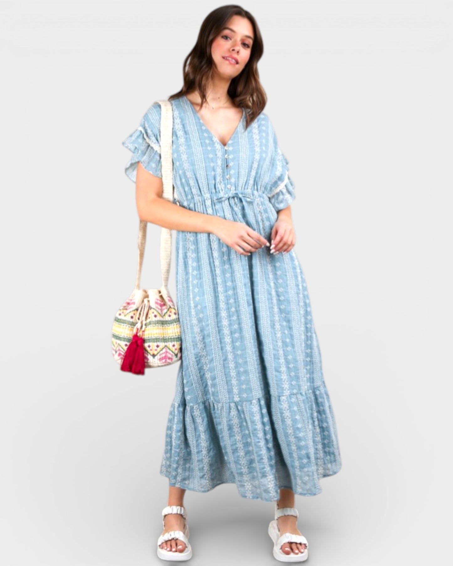Woman wearing a blue striped dress holding a patterned bag on a white background