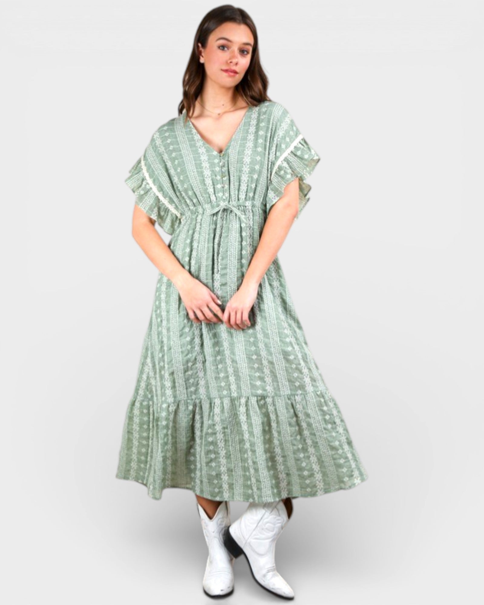 Woman wearing a green patterned dress with white boots on a light gray background